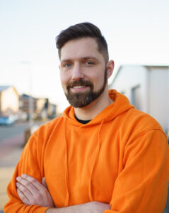 Ein Mann mit Bart und orangenem Kapuzenpulli lächelt in die Kamera